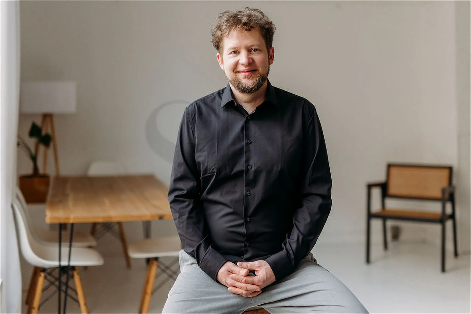 Jos-lammerts-ueber-mich-bild Lächelnder Mann in schwarzem Hemd sitzt in modernem Raum
